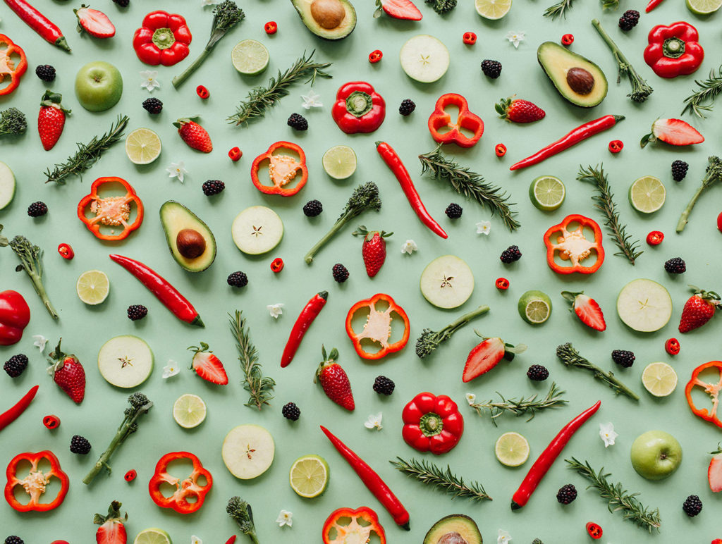 image of various produce including rosemary, tenderstem broccoli, red bell peppers, green apples, red chillis, white flowers, blackberries, strawberries, avocados and limes against a sage green background