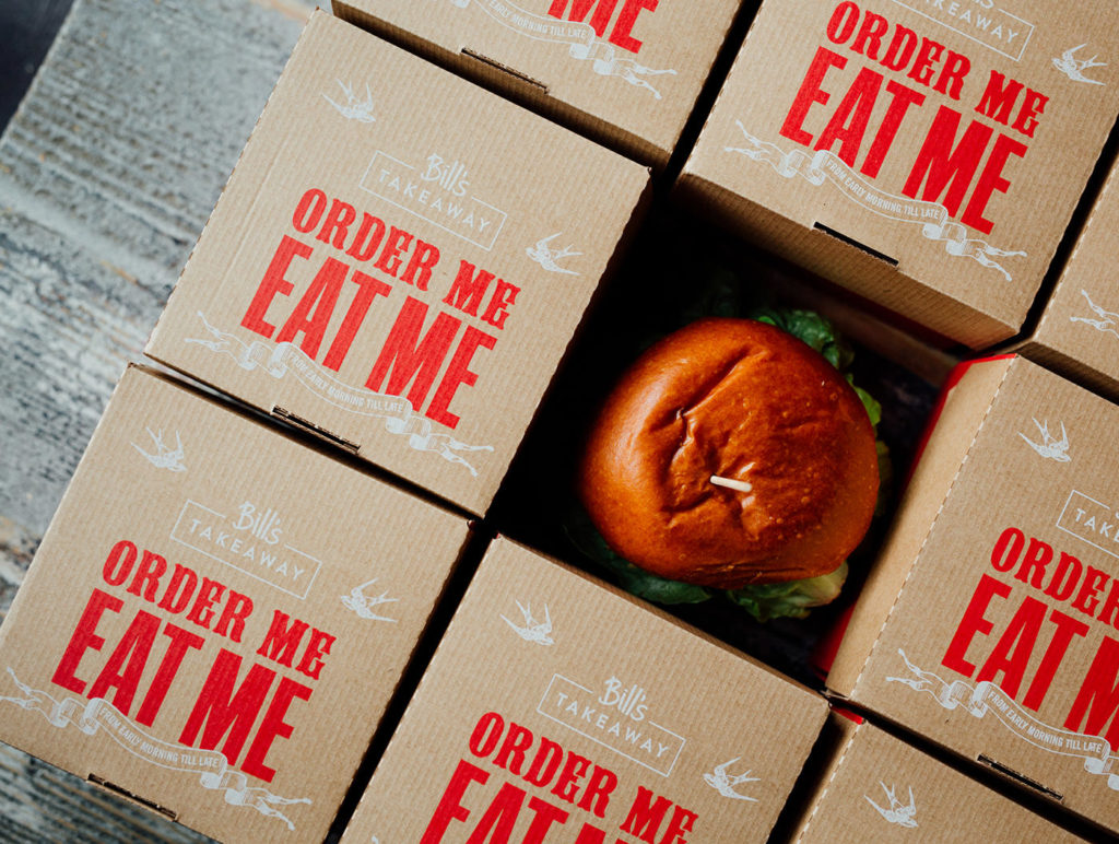 a bird’s eye view of a burger surrounded by burger boxes made of brown carboard with the Bill’s logo in white and red text underneath reading ‘order me, eat me’