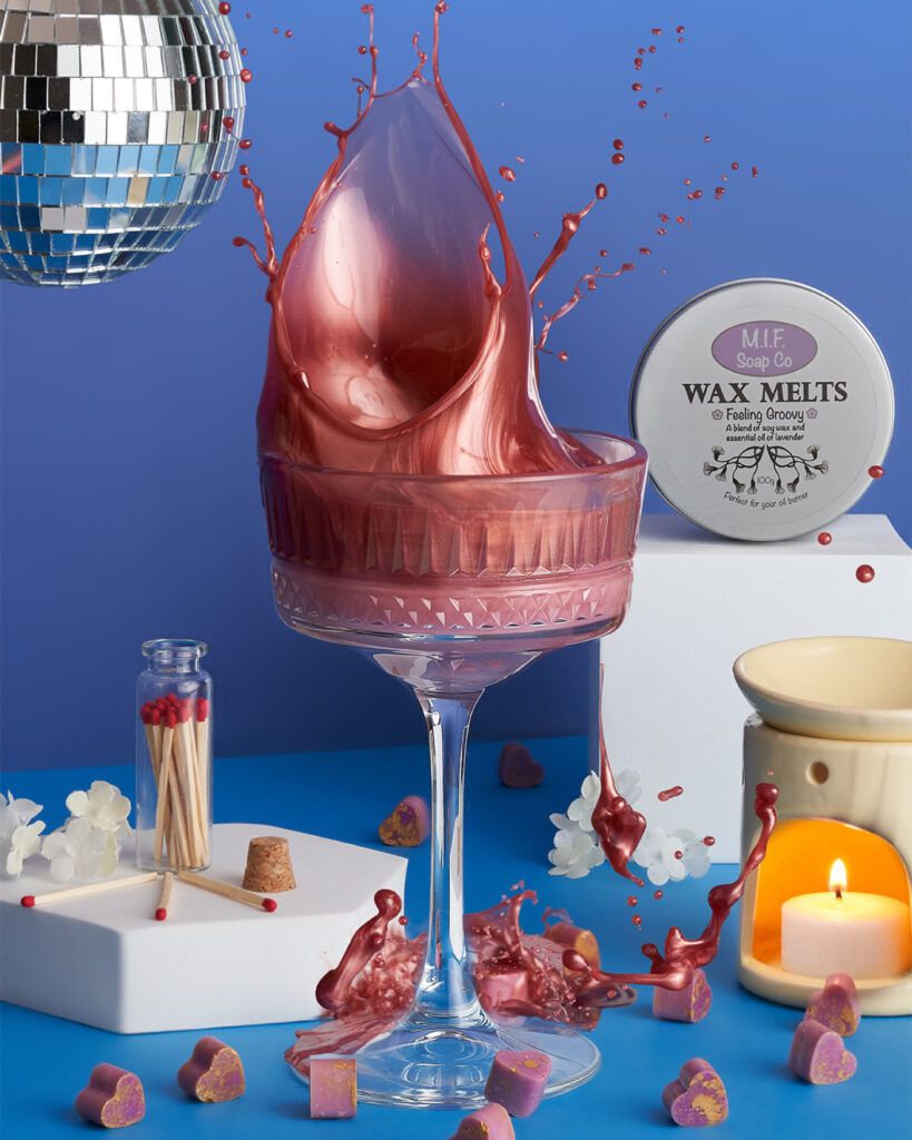 Wax melt in a stemmed glass, surrounded by bits of wax, match sticks, candle warmer and a tin of wax